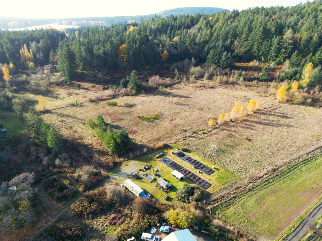 Aerial view of Bear Hill Farm, showing open fields, a small farm building with solar panels, and surrounding forest.