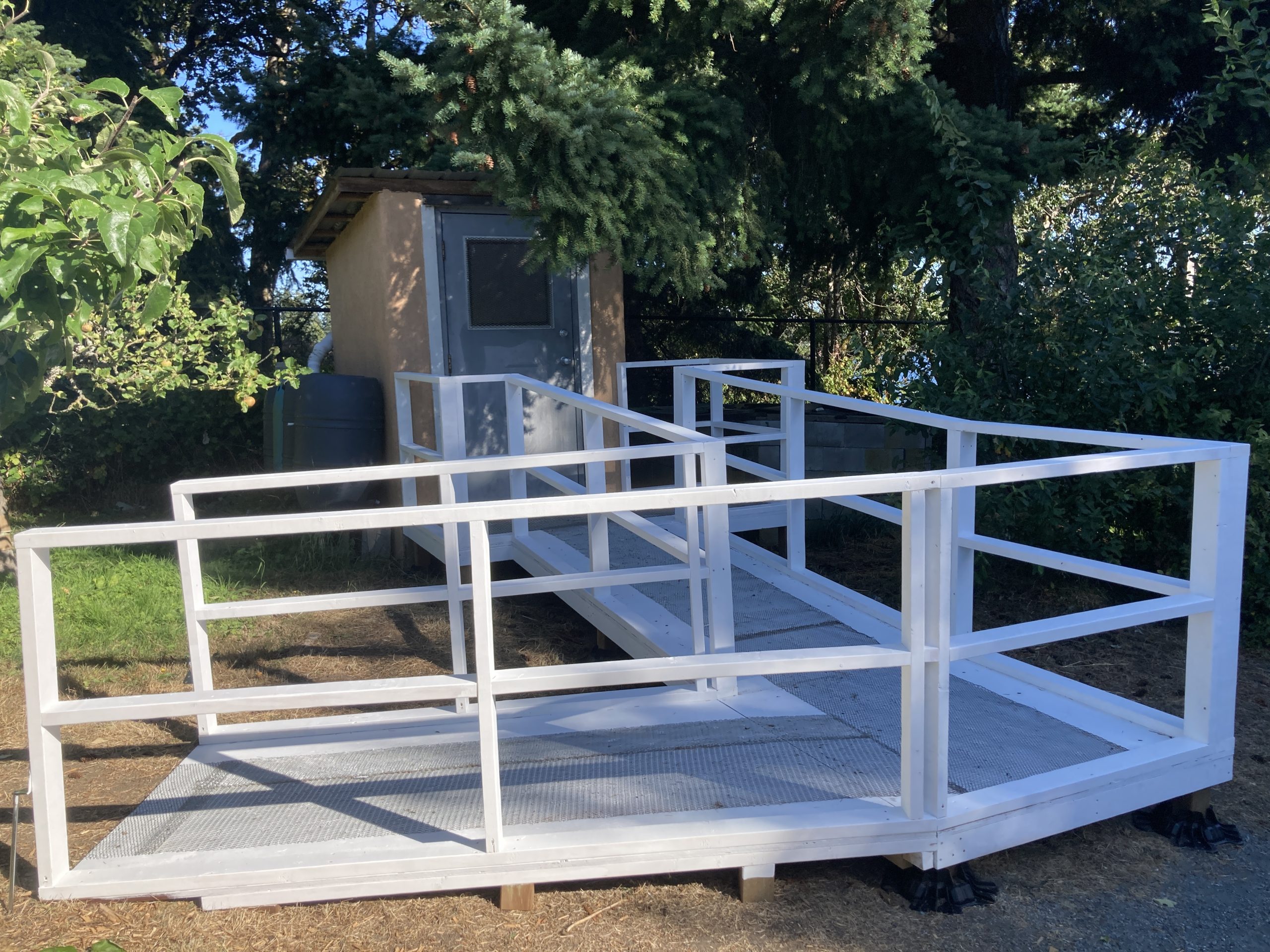 An accessibility ramp with white railings leading up to the bathroom at Welland Community Orchard.