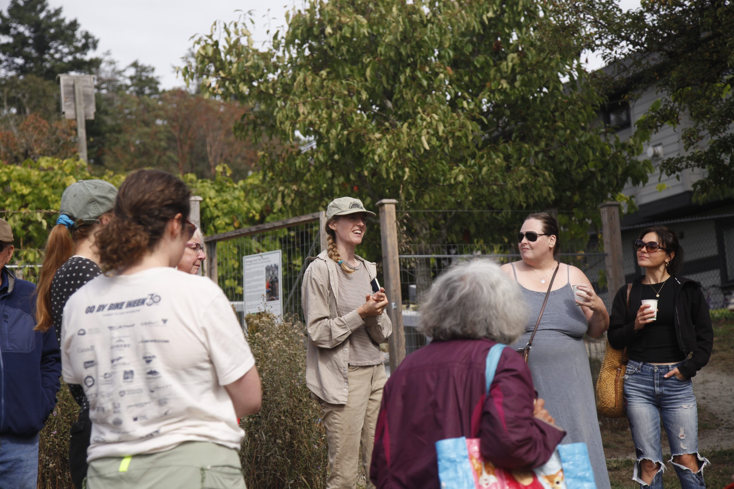 A group of people gathered outdoors at Welland Community Orchard, listening to a staff member leading a discussion.