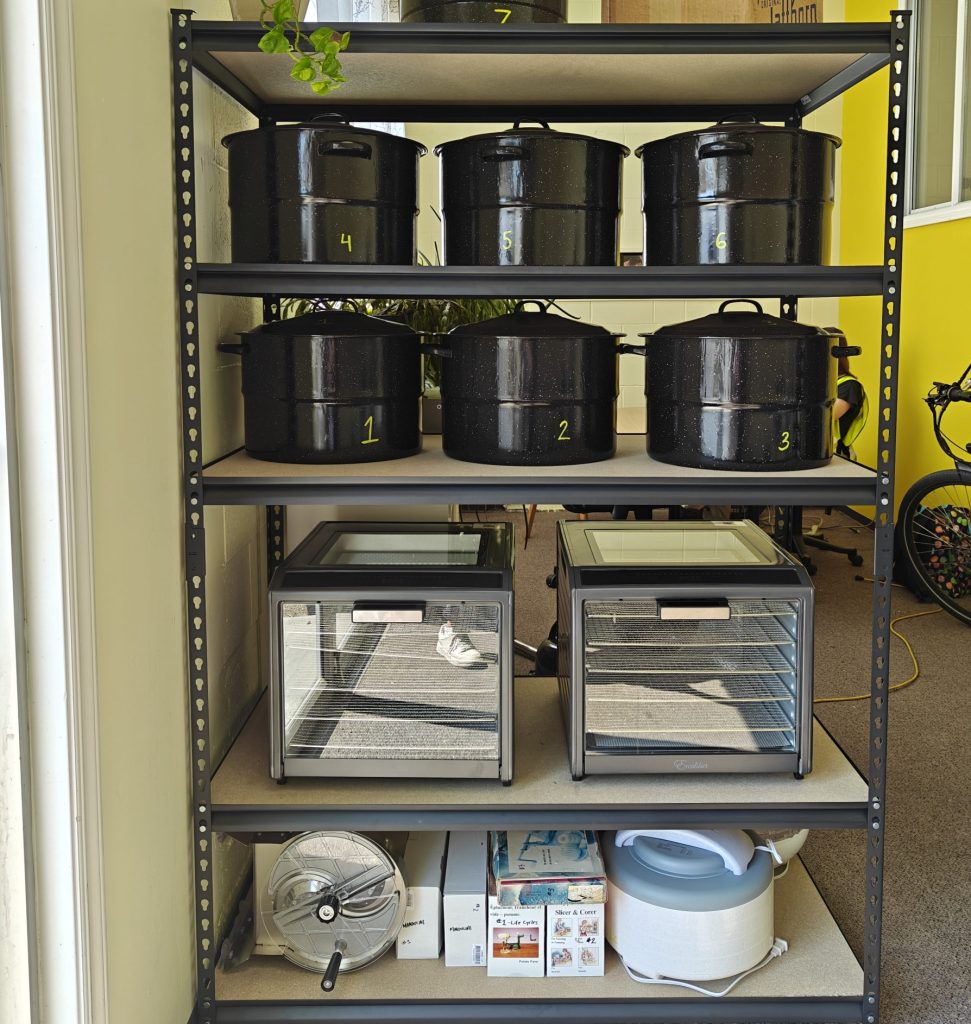 A metal shelving unit stocked with kitchen equipment, including large black pots, food dehydrators, and a slow cooker.