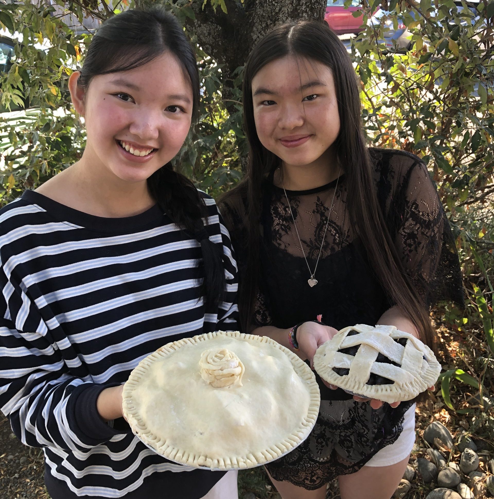 Two youth volunteers smiling as they hold up pies they made at a pie workshop.